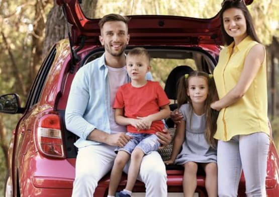 Família sorridente sentada na bagageira aberta de um carro vermelho